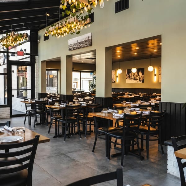 Spacious, modern restaurant interior with numerous wooden tables, black chairs, and large windows.