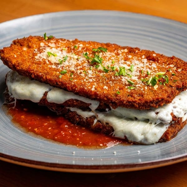 Crispy fried eggplant parmesan with melted mozzarella, marinara sauce, and fresh parsley on a blue plate.