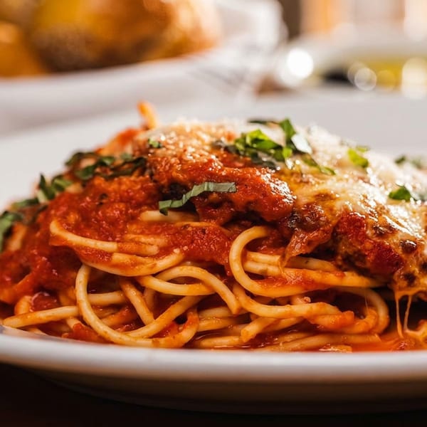 Spaghetti with red sauce, melted cheese, and fresh basil on a white plate.