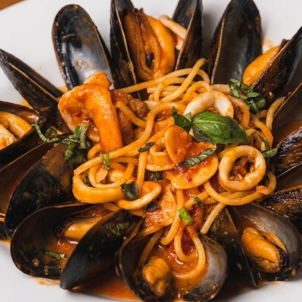 Spaghetti with mussels, calamari, and shrimp in a rich tomato sauce, garnished with basil.