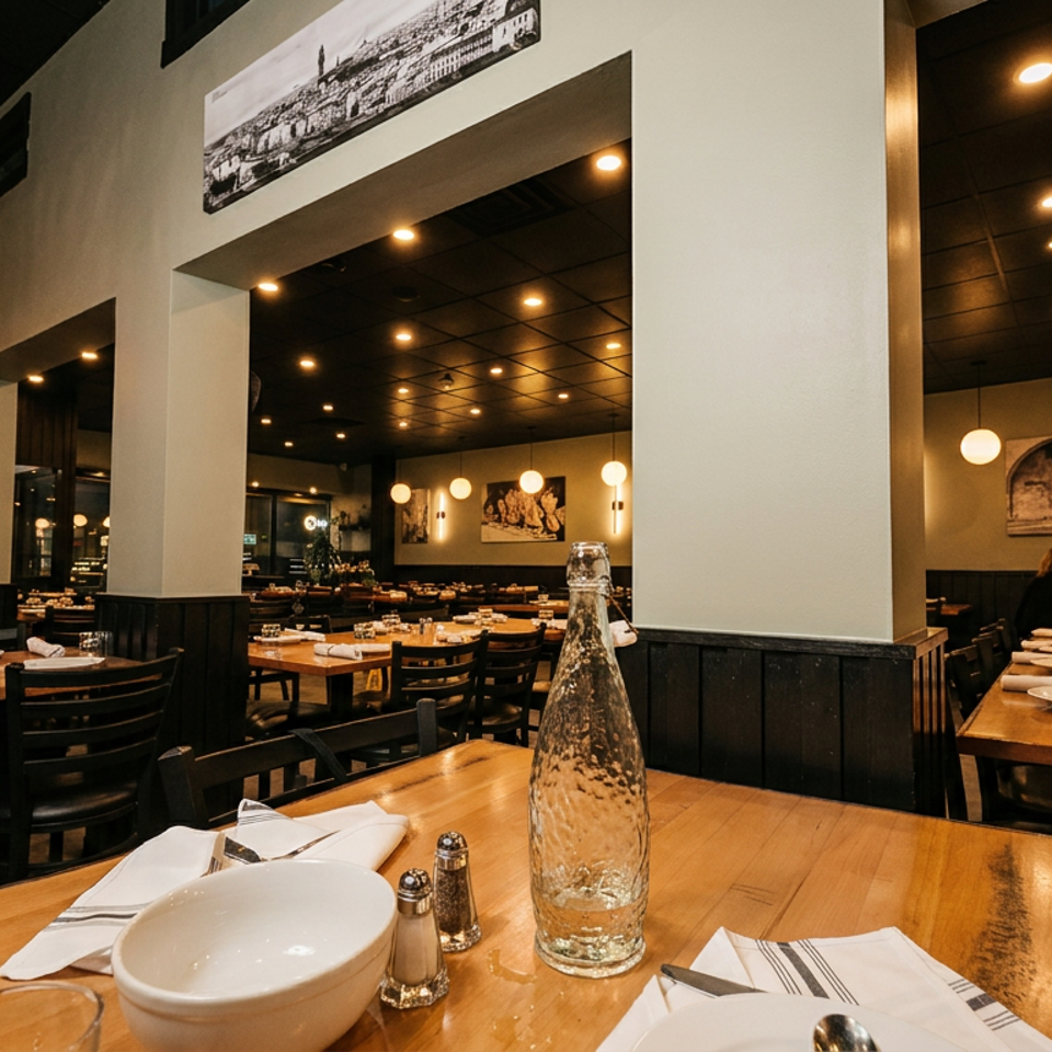 Warmly lit restaurant interior with wooden tables, set with white dishes, and dark chairs.