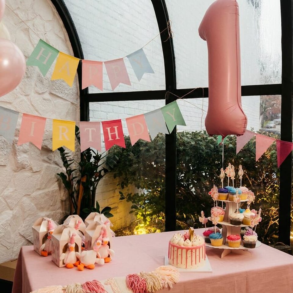 A pink-themed first birthday party setup with cake, cupcakes, balloons, and a "HAPPY BIRTHDAY" banner.