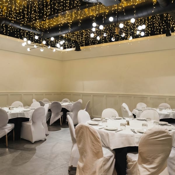 Elegant dining room with round tables, white chairs, and a ceiling adorned with string lights.