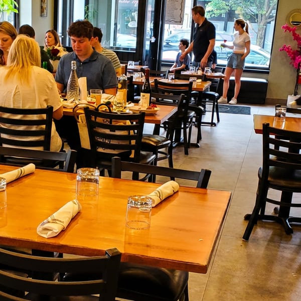 A bustling restaurant interior with patrons dining at wooden tables and staff moving through the space.