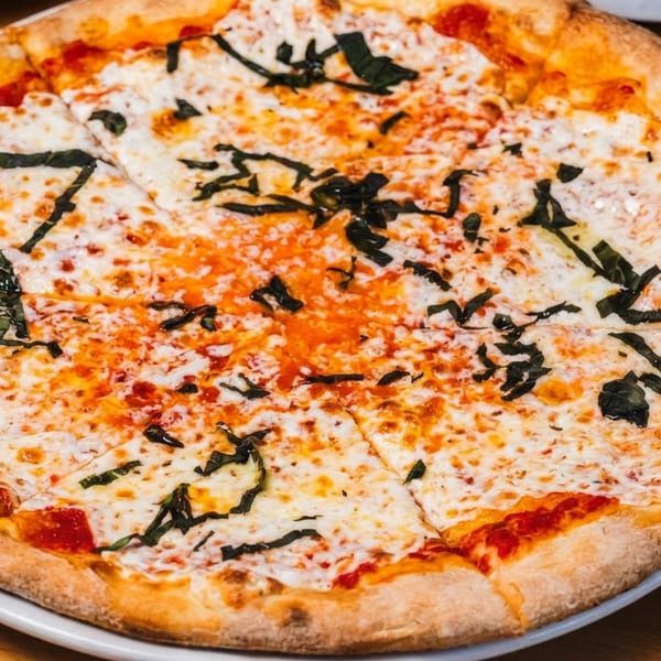 A freshly baked, sliced Margherita pizza with melted cheese and basil on a white plate.