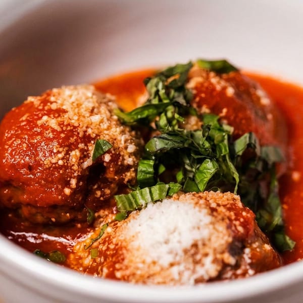 Meatballs in red sauce, topped with grated cheese and fresh basil, served in a white bowl.