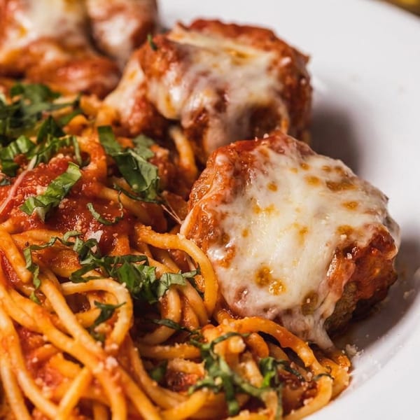Spaghetti and meatballs with melted cheese and fresh basil on a white plate.